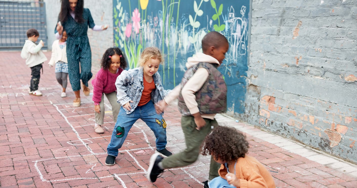 Hopscotch, kids and playing with outdoor game at Kindergarten for childhood development. Group, children or learners jumping with teacher for fun activity, hopping or skipping on school playground stock photo
